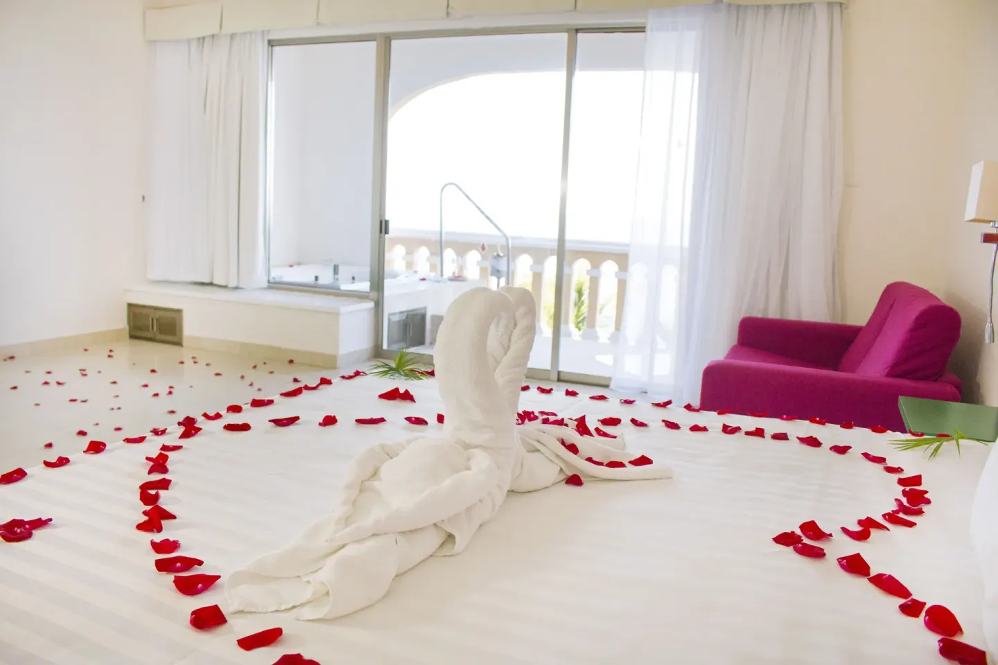 Bed with towel swans and rose petals in a guest room at All Ritmo Cancun Resort & Water Park.