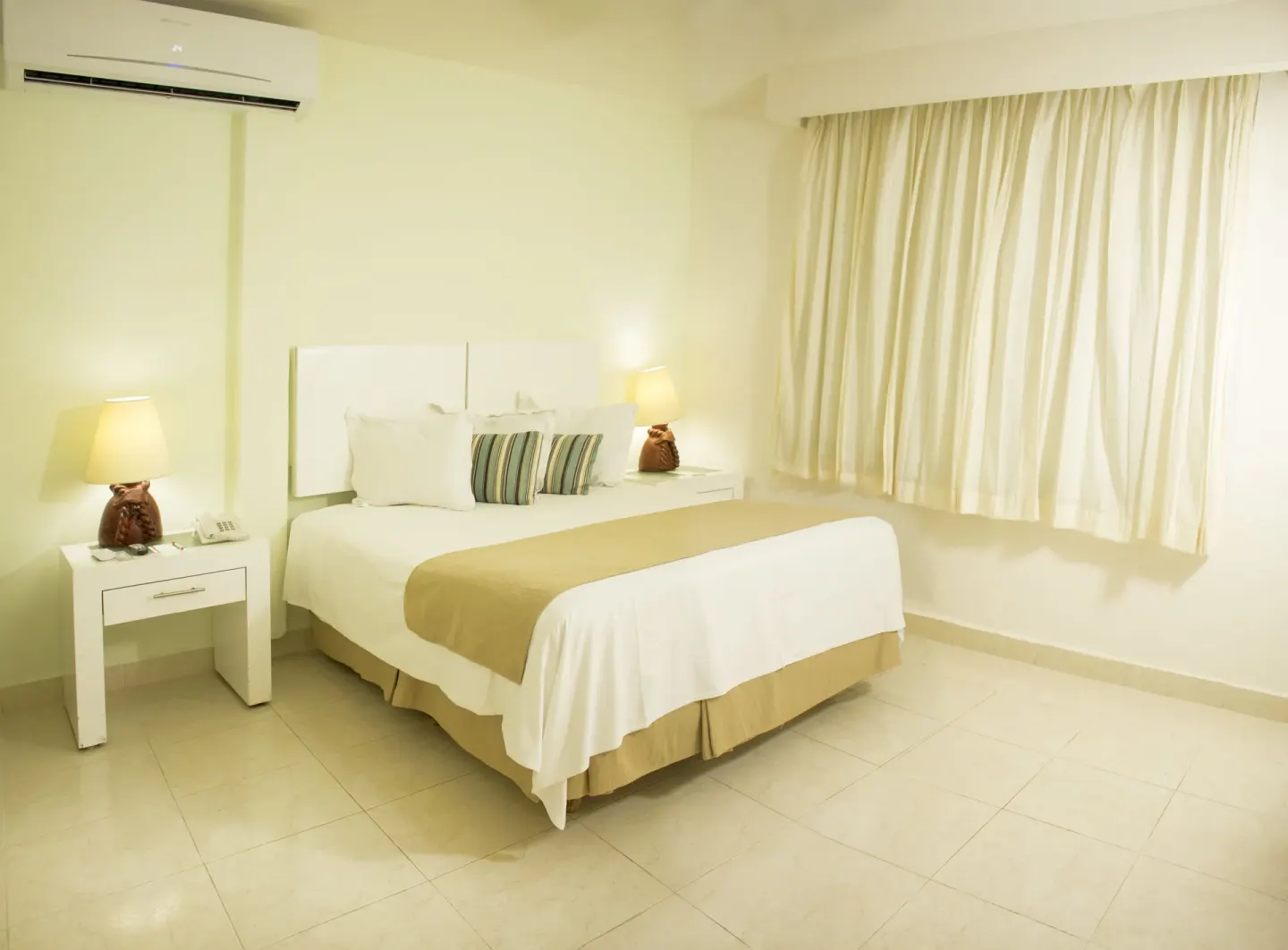 King bed with bedside lamps and cream curtains at All Ritmo Cancun Resort & Water Park.