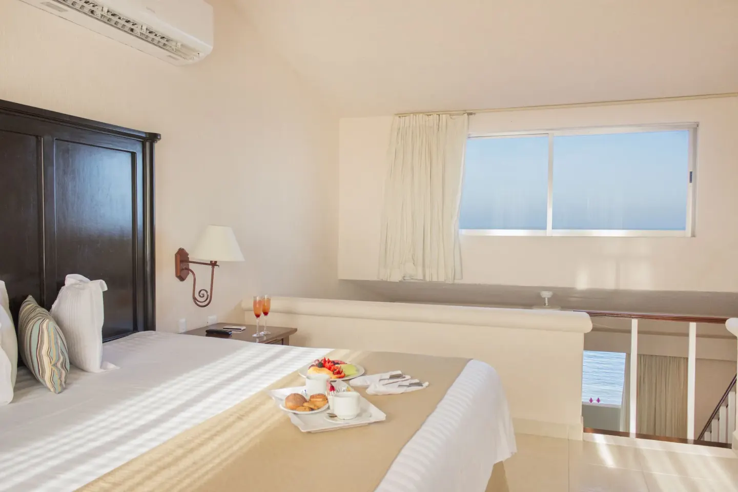 Loft-style king bed with breakfast tray and ocean-facing window at All Ritmo Cancun Resort & Water Park.