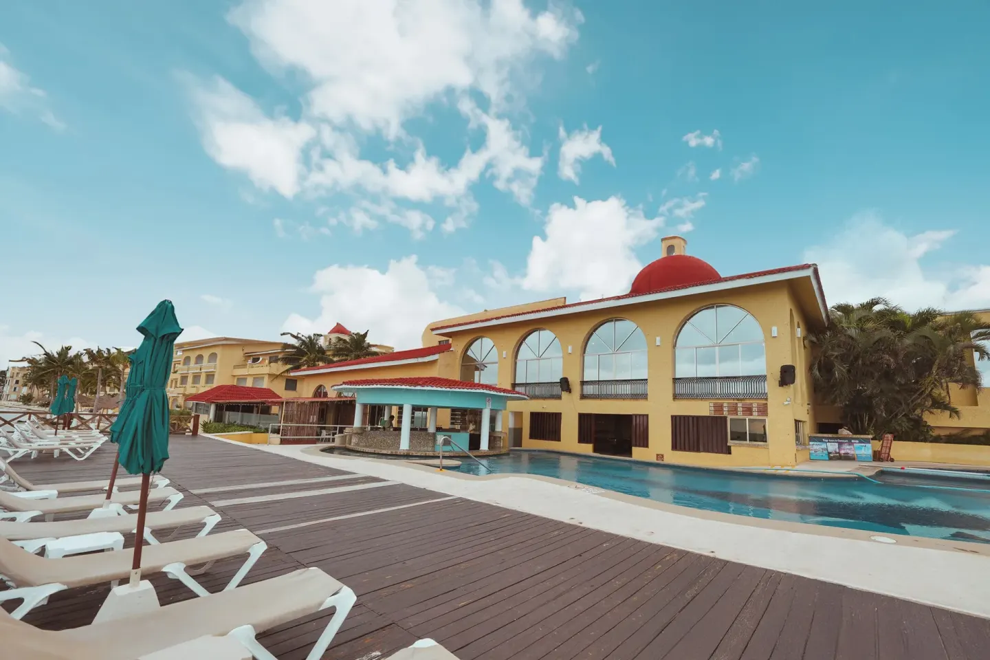 Pool deck and yellow building with arched windows at All Ritmo Cancun Resort & Water Park.
