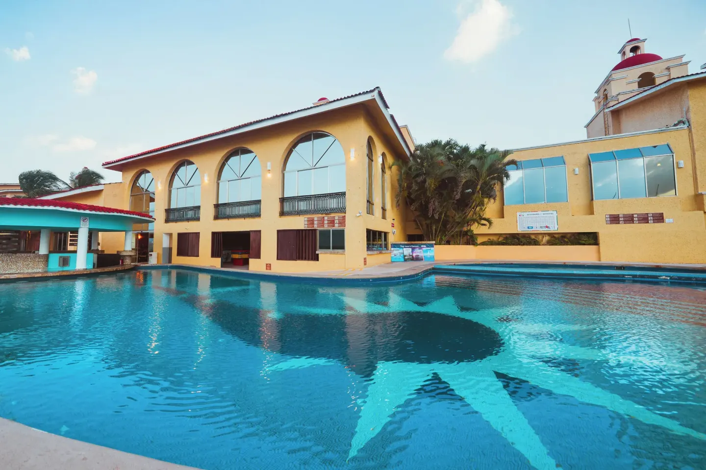 Large pool with star pattern beside resort buildings at All Ritmo Cancun Resort & Water Park.