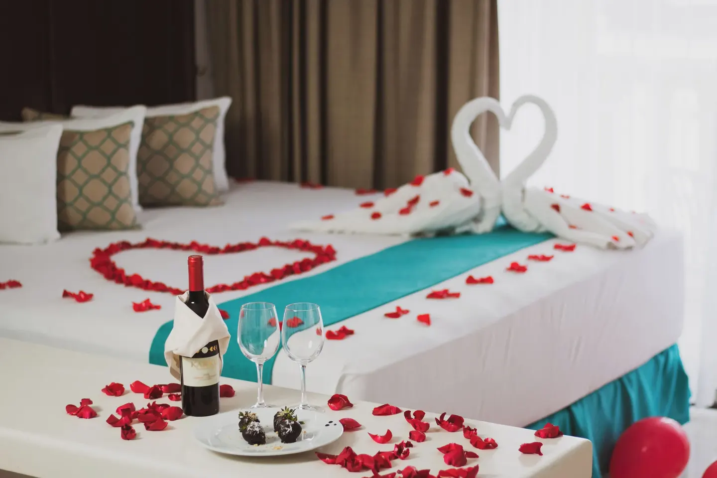Romantic king bed setup with rose petals and towel swans at All Ritmo Cancun Resort & Water Park.