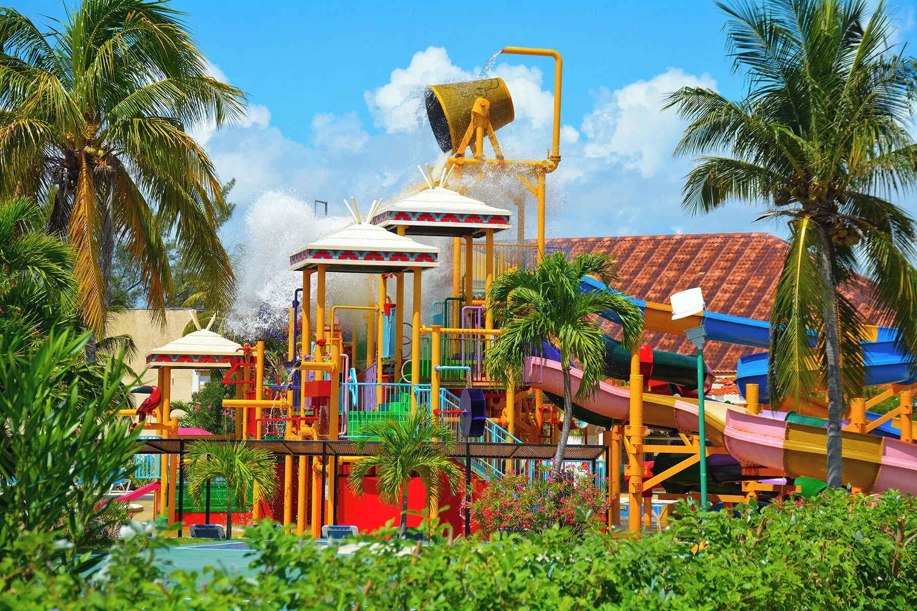 Tipping bucket and colorful slides among palms at All Ritmo Cancun Resort & Water Park.