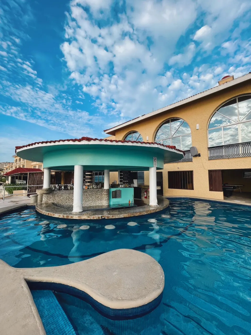 Swim-up pool bar at All Ritmo Cancun Resort & Water Park beneath a turquoise roof by the water.