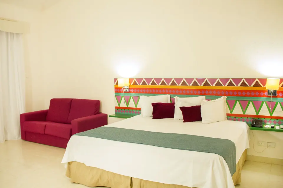 Junior Suite Sea View king bed and red sofa at All Ritmo Cancun Resort & Water Park.