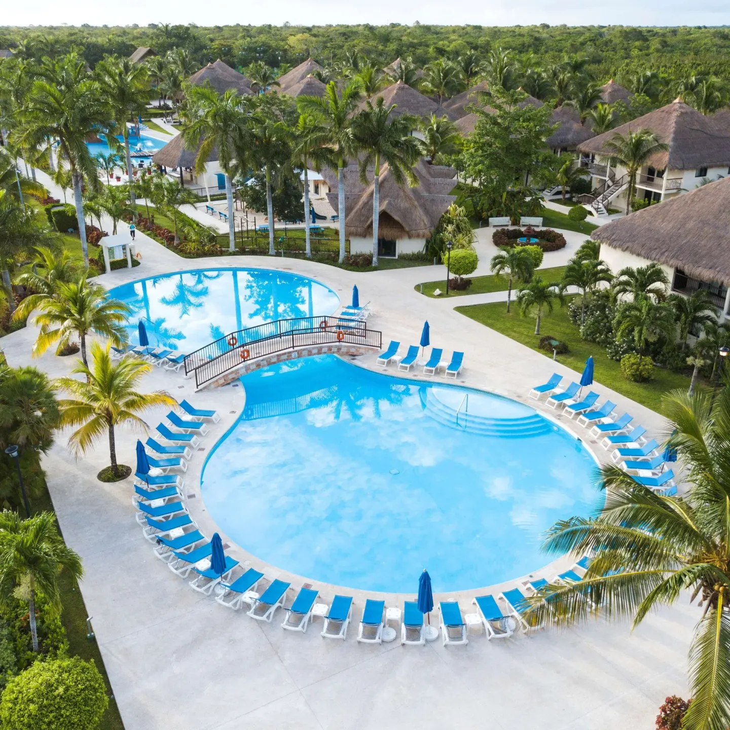Aerial view of a round pool, loungers, palms, and thatched buildings at Allegro Cozumel.