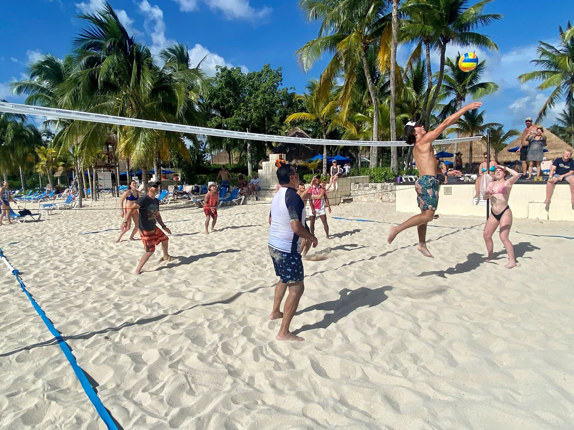 Guests play beach volleyball on the sand at Allegro Cozumel under palm trees.