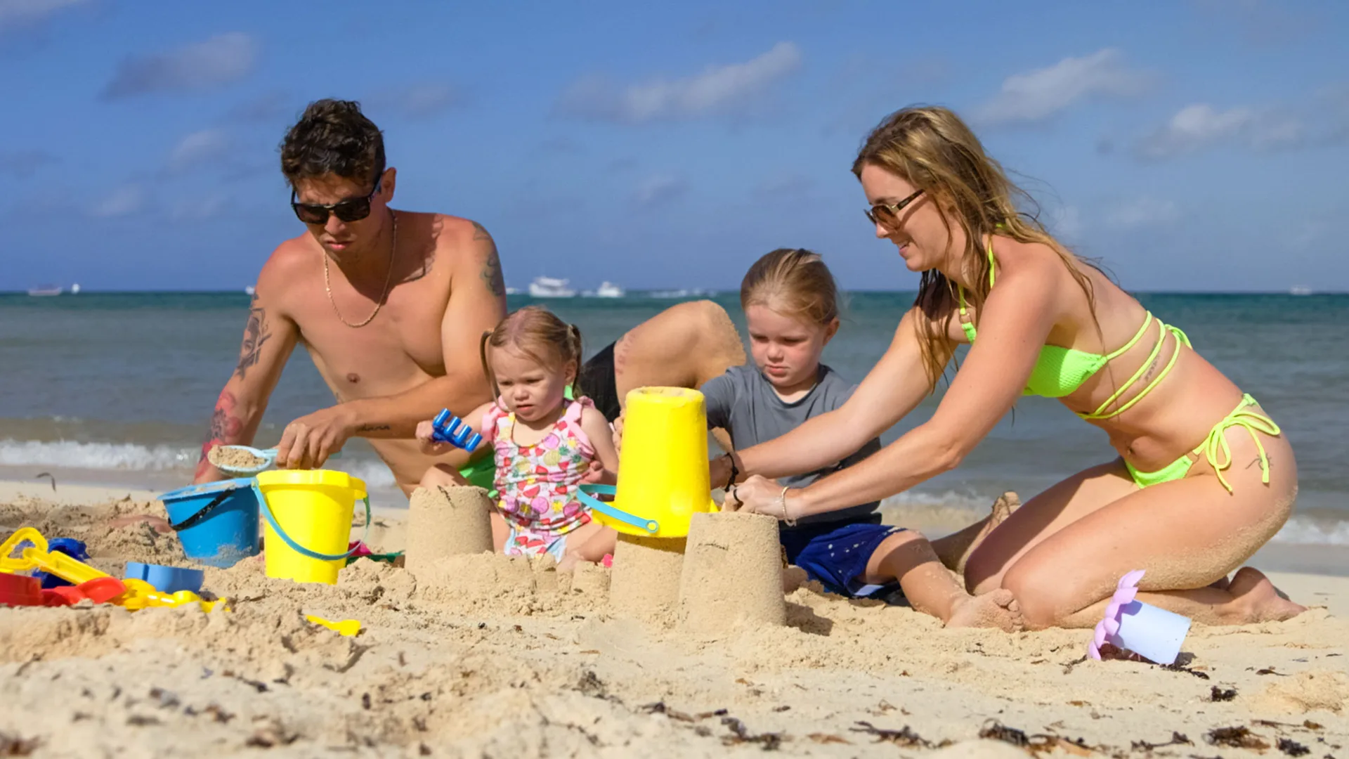 Family builds sandcastles on the beach at Allegro Cozumel with the sea behind them.