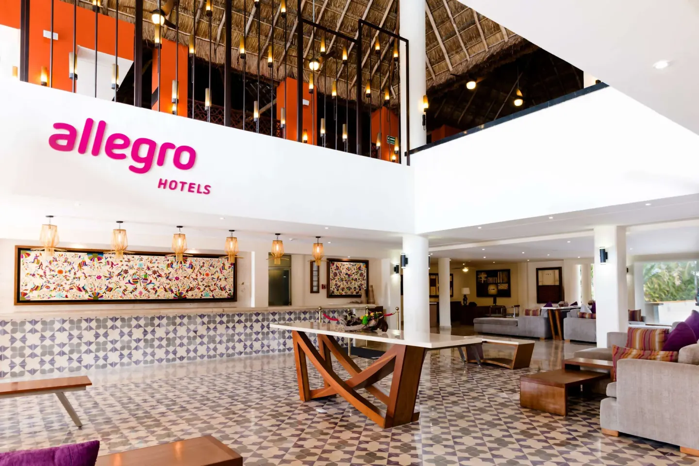 Open lobby with Allegro sign, patterned tile, sofas and thatched ceiling at Allegro Cozumel.