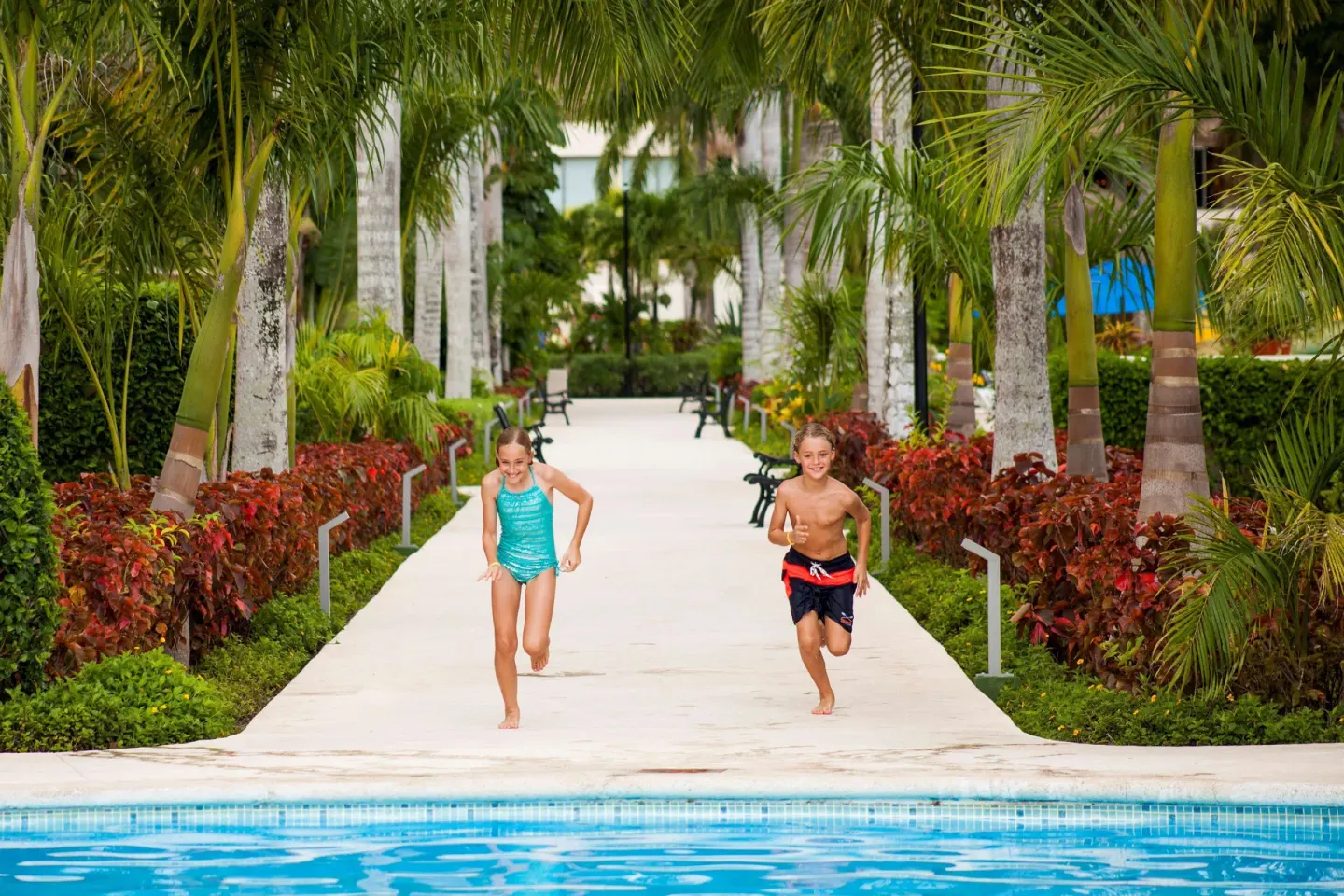 Children run along a palm-lined walkway beside the pool at Allegro Cozumel.