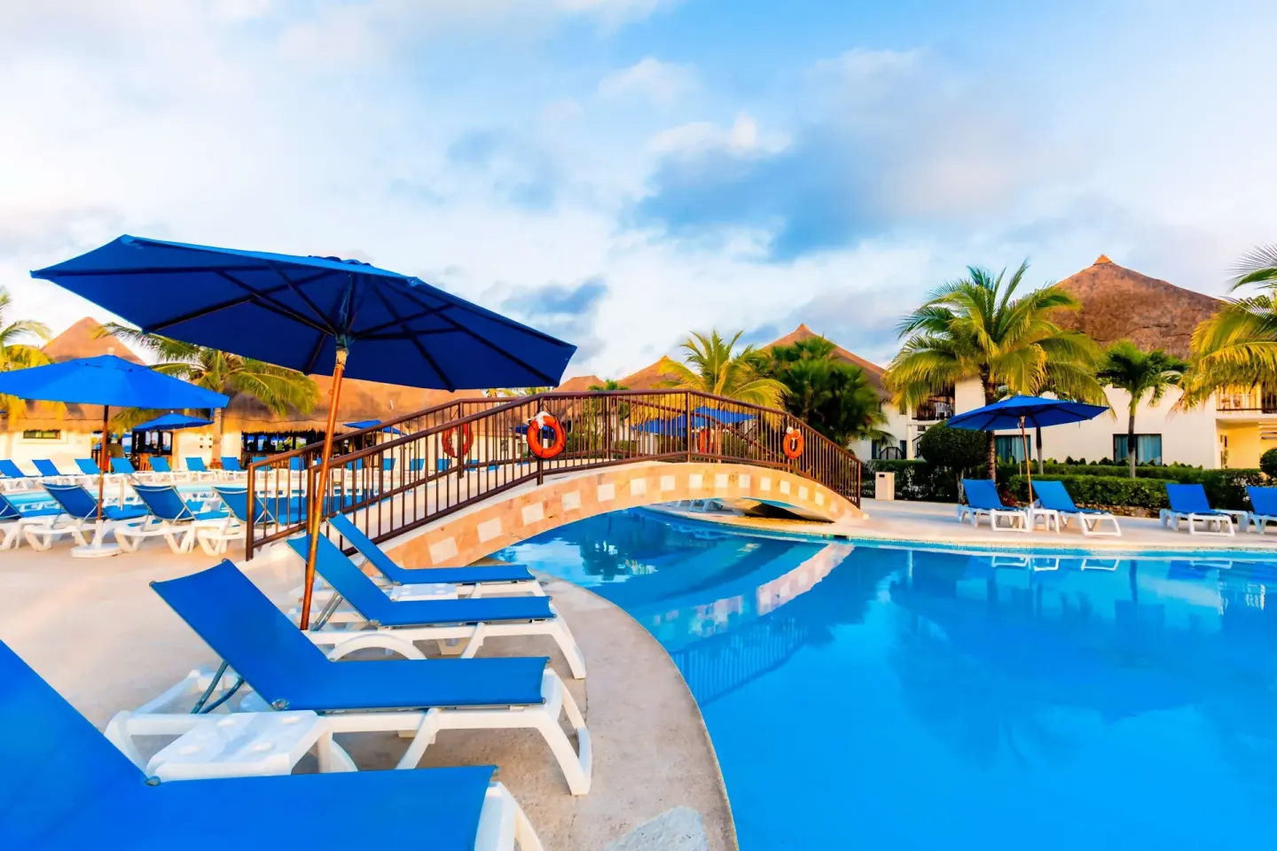 Blue loungers and umbrellas line a pool with a small arched bridge at Allegro Cozumel.