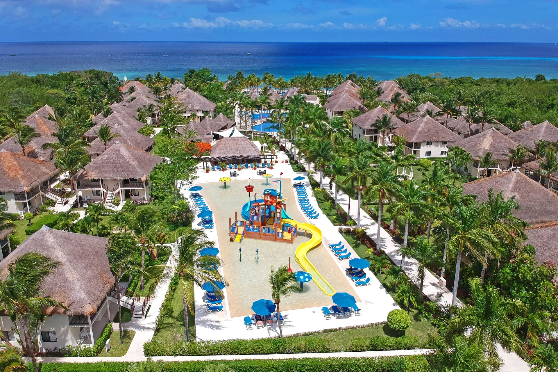 Aerial view of the splash pool area and thatched buildings near the sea at Allegro Cozumel.