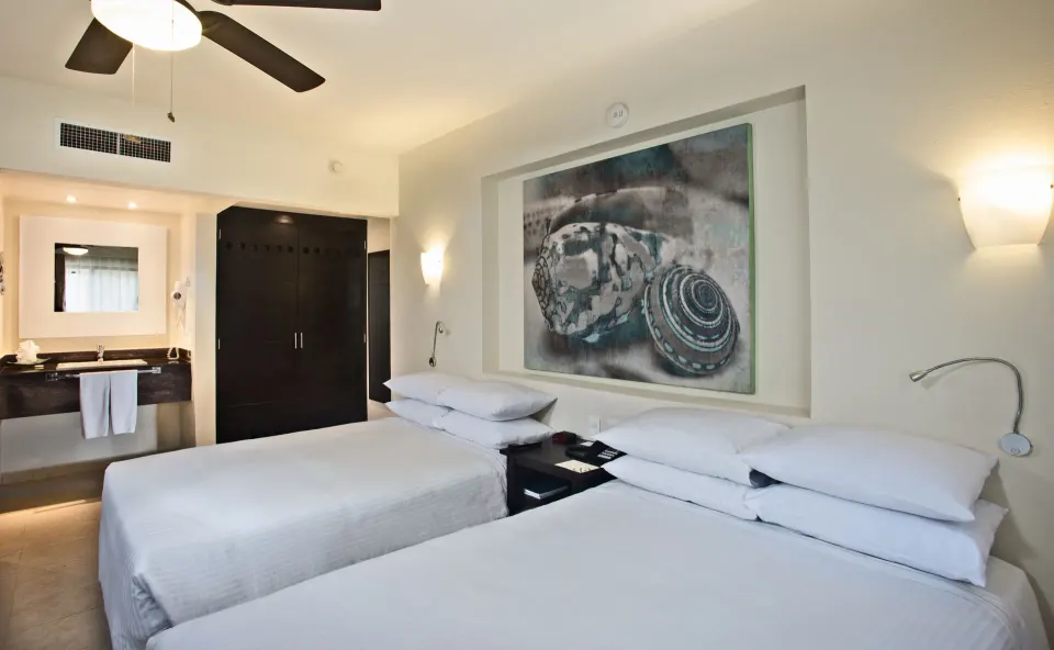 Family Room Garden View with two beds, vanity area, and shell artwork at Allegro Cozumel.