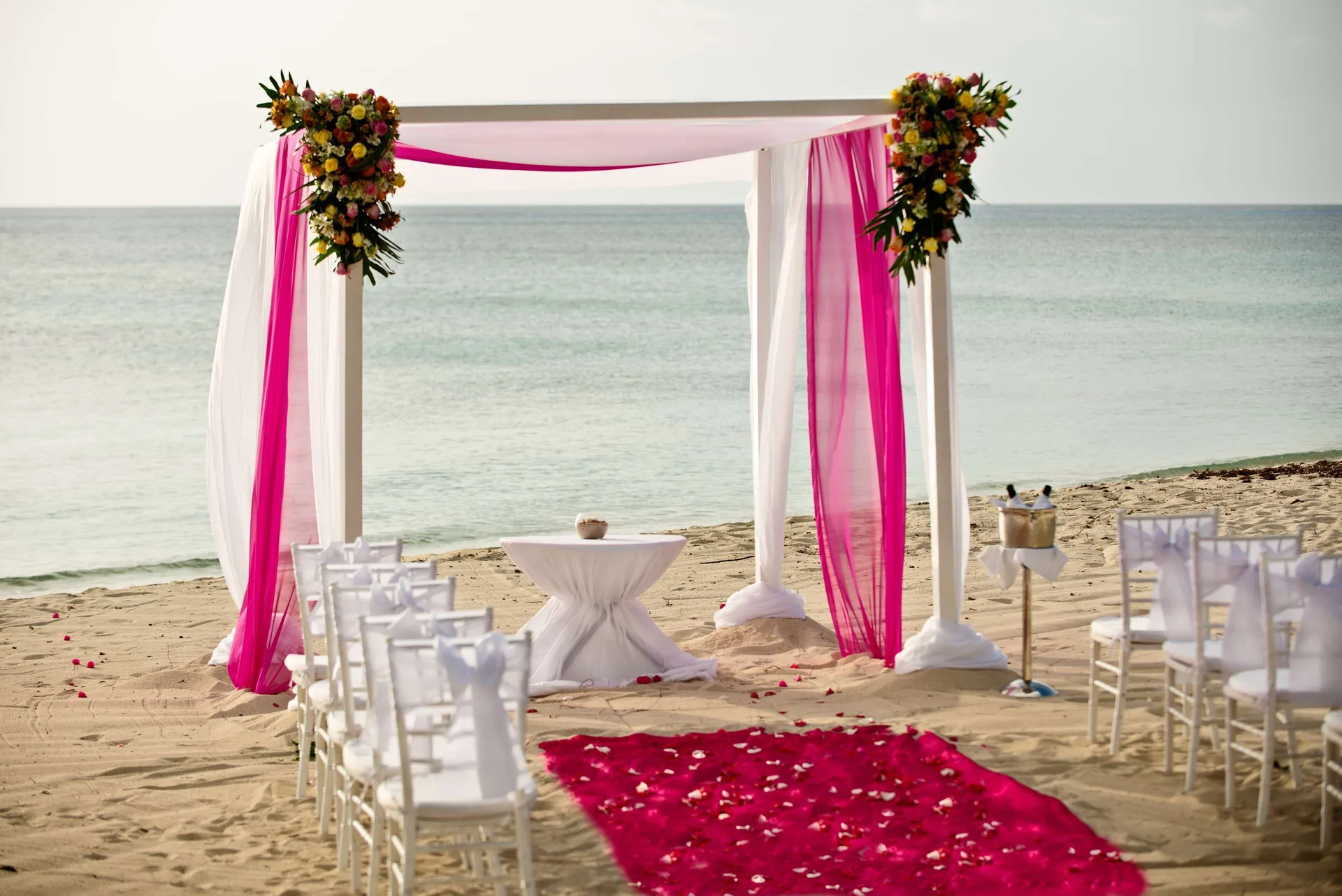 Pink and white beach wedding arch with chairs by the water at Allegro Cozumel.