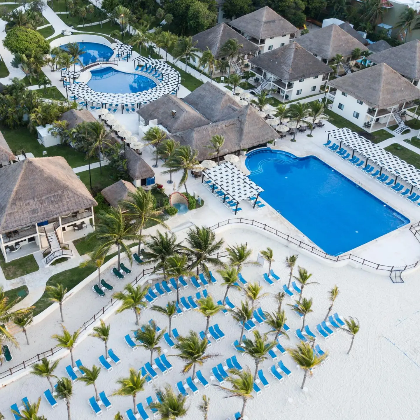 Aerial view of pools, beach loungers, palms, and thatched buildings at Allegro Playacar.