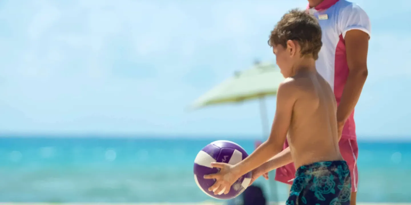 A child holds a ball during a beach activity at Allegro Playacar.