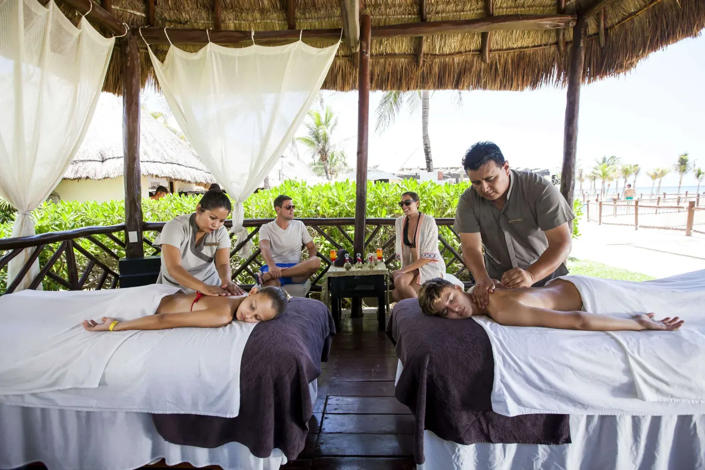 Two guests receive side-by-side massages in a thatched pavilion at Allegro Playacar.