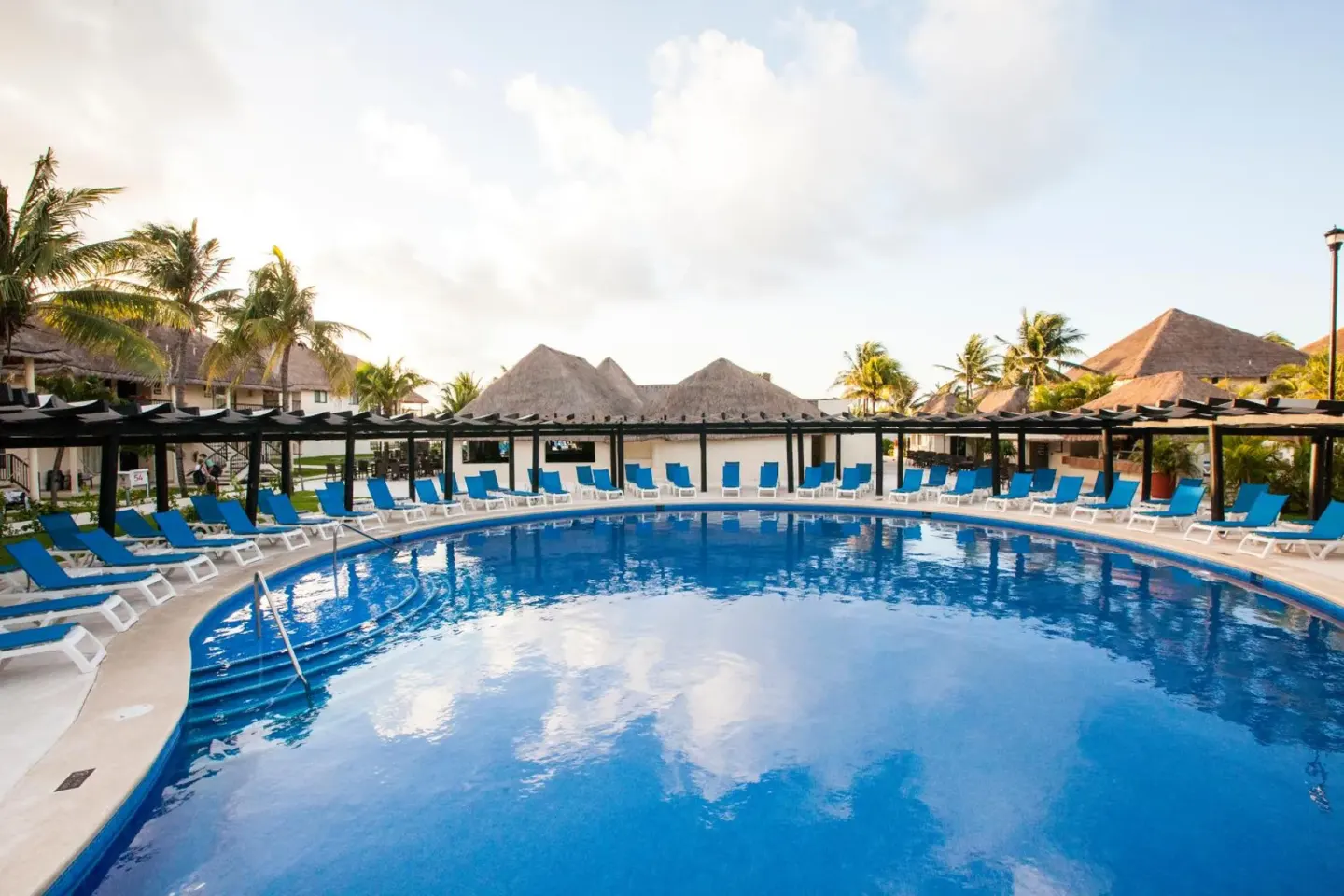 Curved pool with blue loungers and thatched buildings at Allegro Playacar.