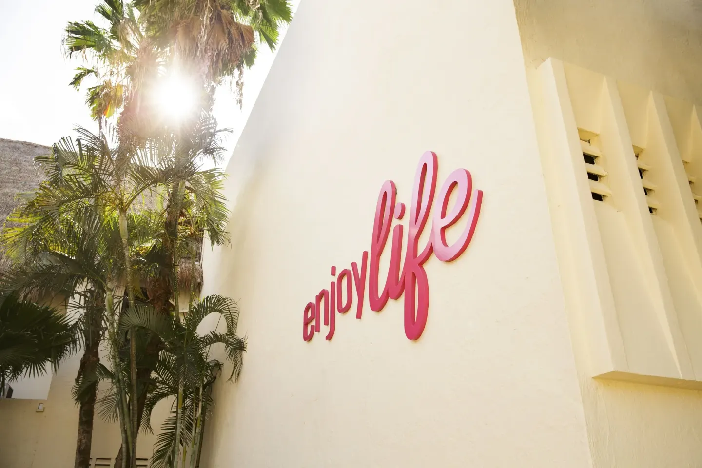 Exterior wall with a pink “enjoy life” sign and palms at Allegro Playacar.