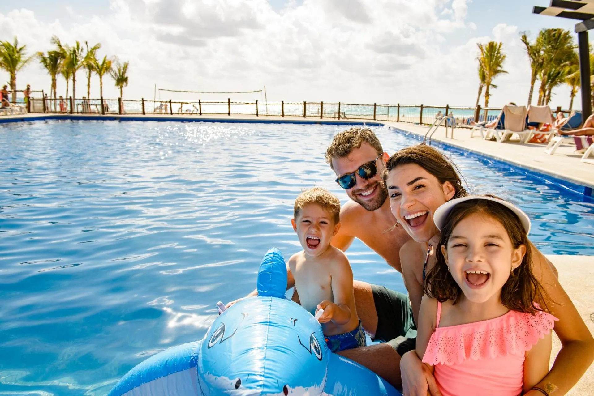 Family smiling beside a pool with an inflatable dolphin at Allegro Playacar.