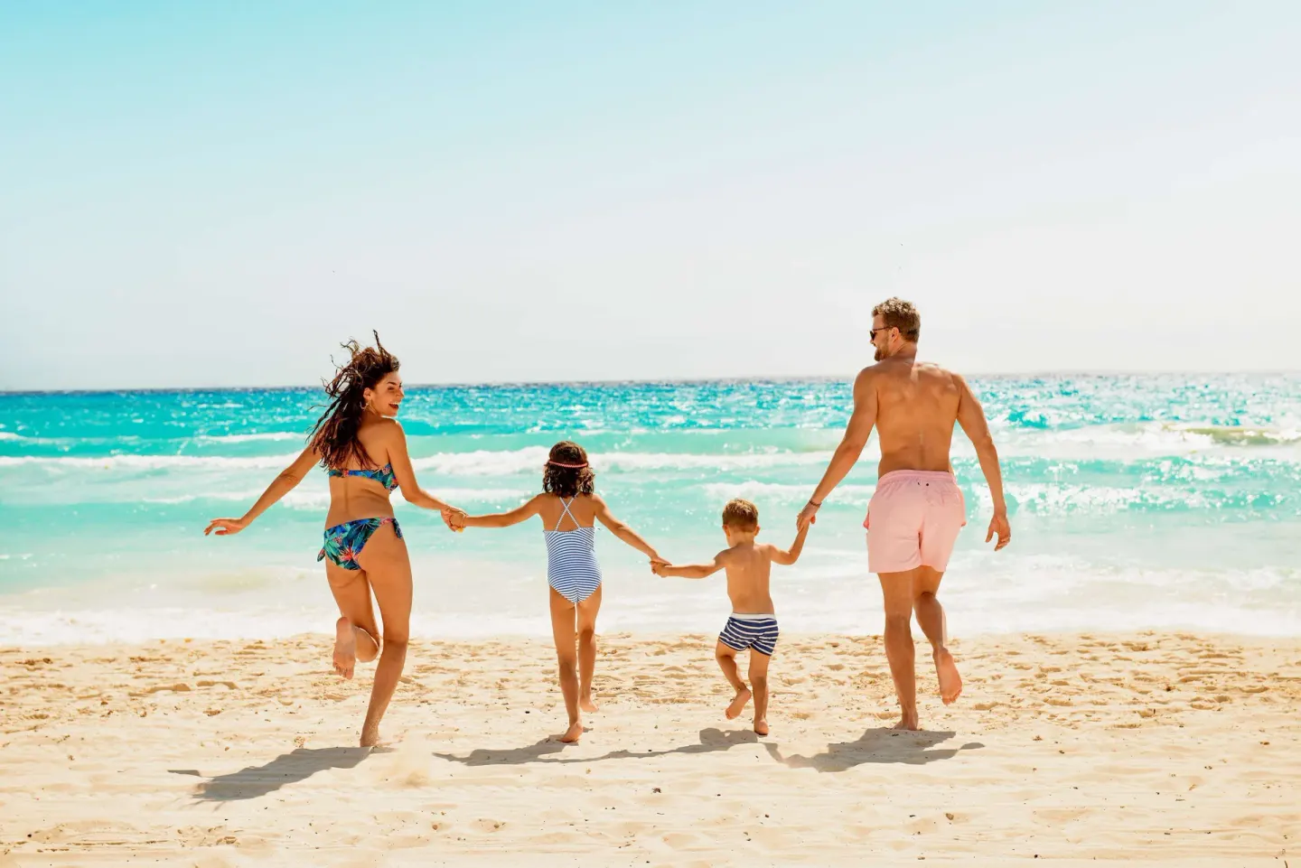 A family runs hand in hand toward the ocean at Allegro Playacar.