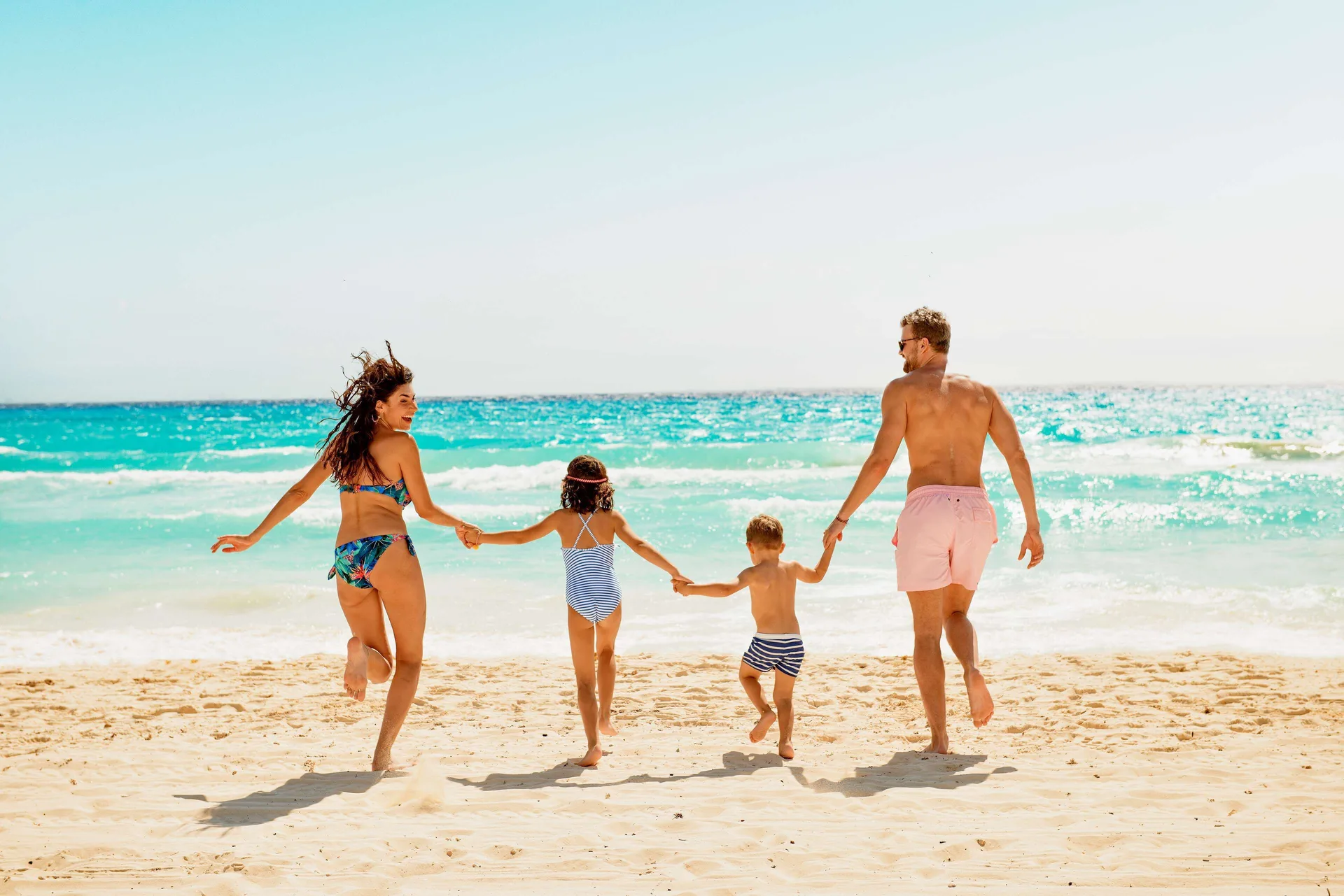 A family runs hand in hand toward the ocean at Allegro Playacar.