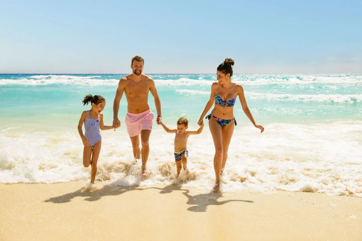 A family walks through shallow surf on the beach at Allegro Playacar.