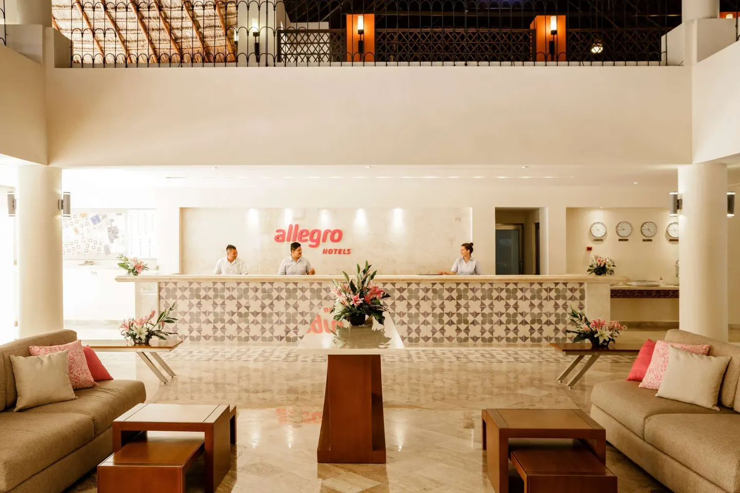 Lobby reception desk with staff, sofas, flowers, and wall clocks at Allegro Playacar.