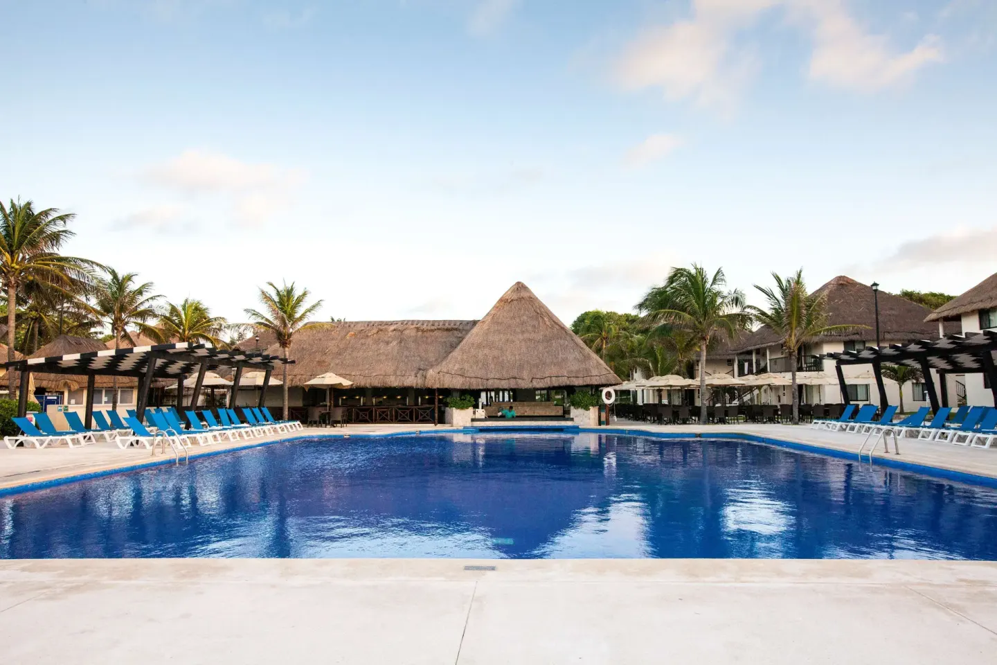 Main pool with blue loungers, thatched roofs, and palms at Allegro Playacar.