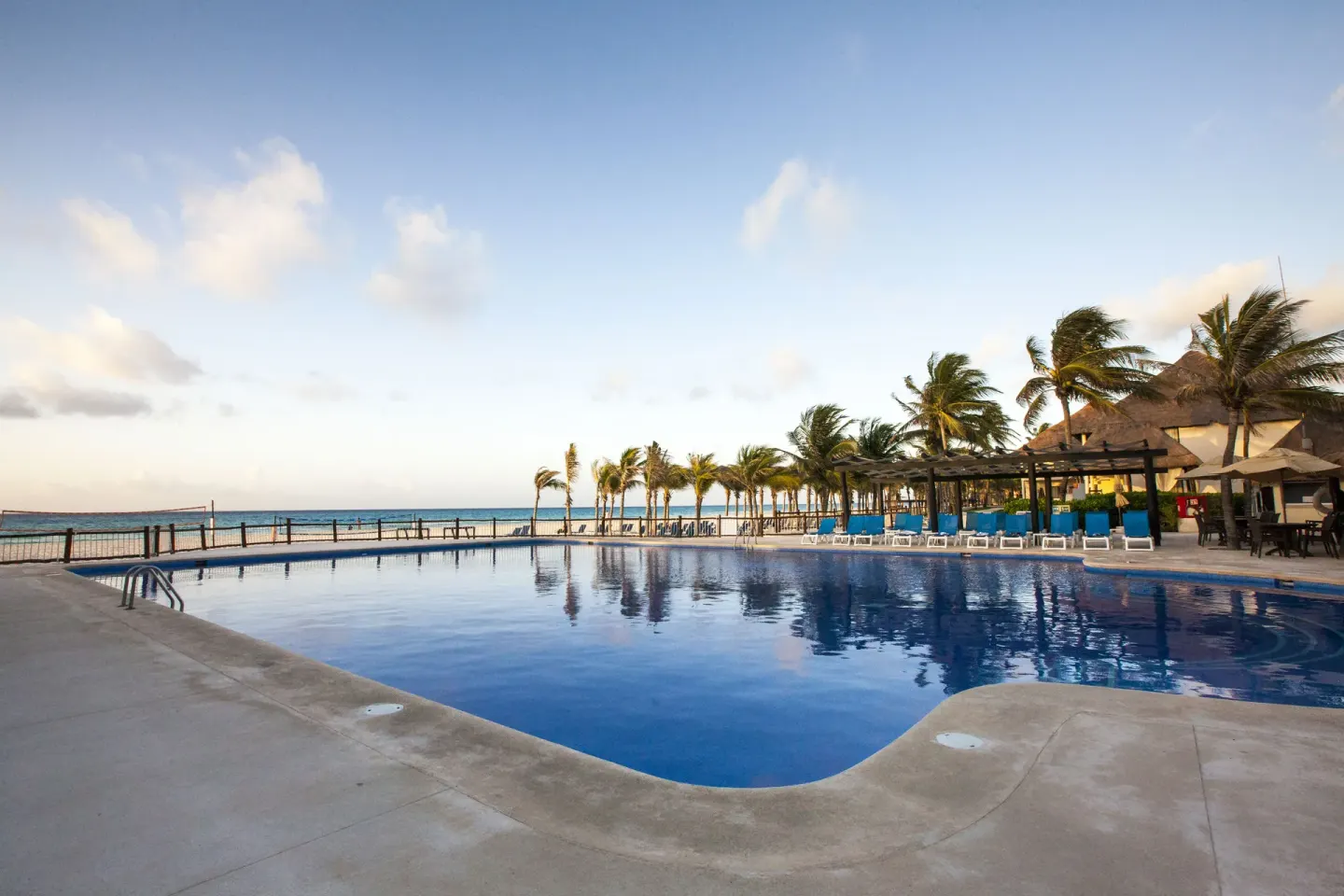 Oceanfront pool with palm trees, lounge chairs, and the sea beyond at Allegro Playacar.