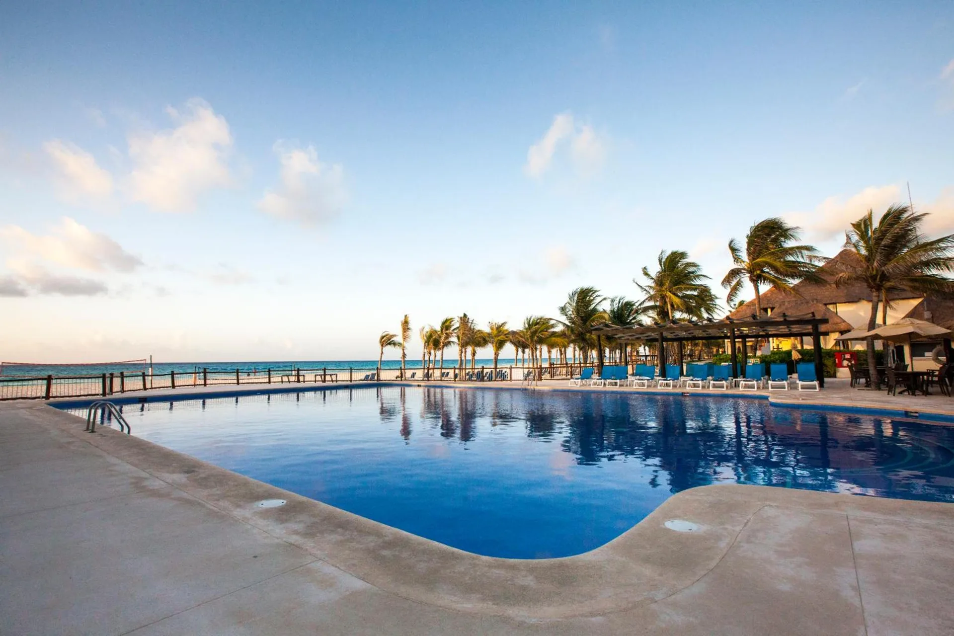 Oceanfront pool with palm trees, loungers, and beach beyond at Allegro Playacar.