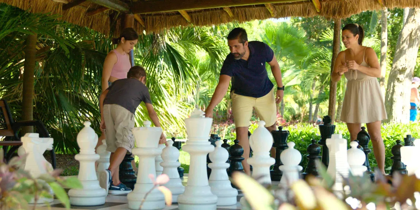 Family plays oversized chess under a thatched shelter at Allegro Playacar.