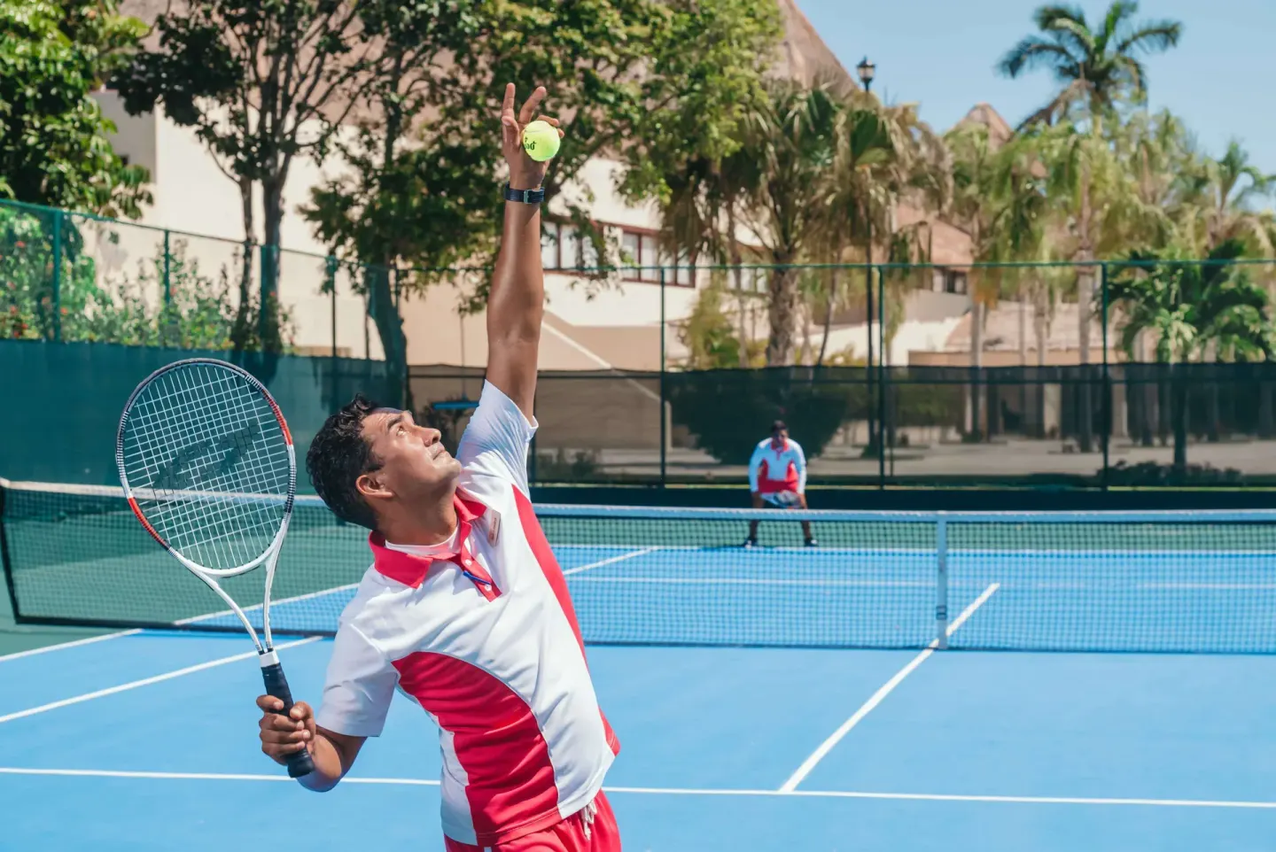 A tennis player serves on a blue court at Allegro Playacar.