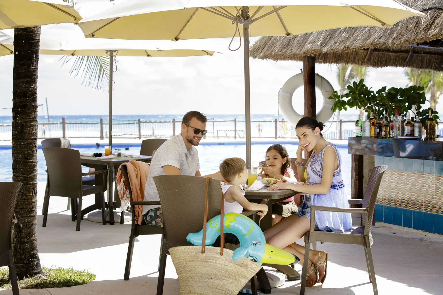 Family seated beside a beachfront bar and pool at Allegro Playacar.