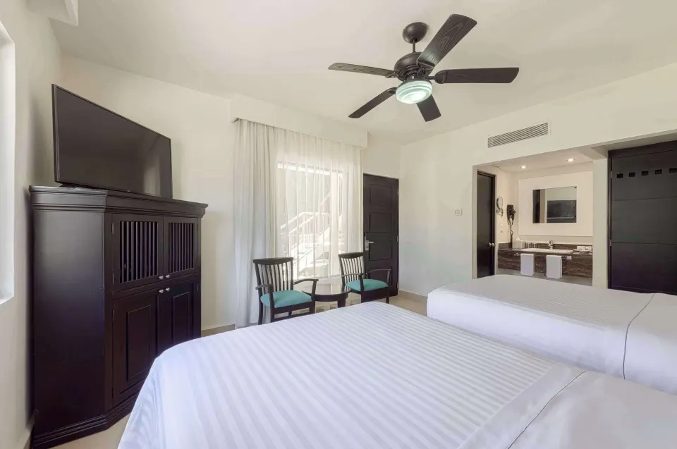 Premium Room with two beds, TV cabinet, chairs, ceiling fan, and vanity area at Allegro Playacar.