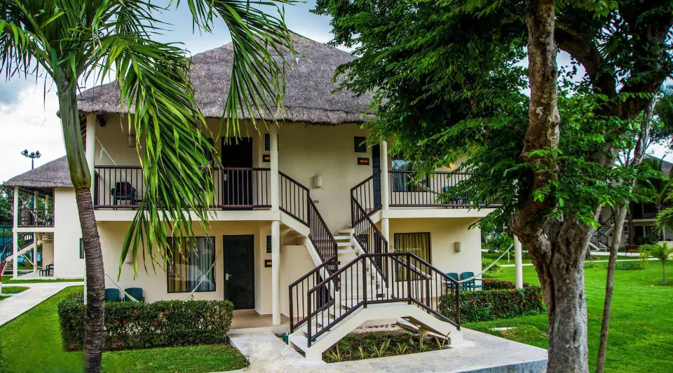 Superior Room building with thatched roof, balconies, stairs, and gardens at Allegro Playacar.