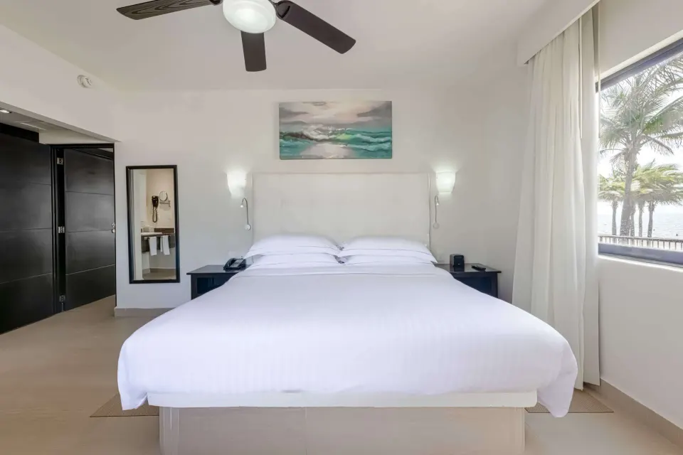 Superior Room king bed with window, palm trees, and wall sconces at Allegro Playacar.