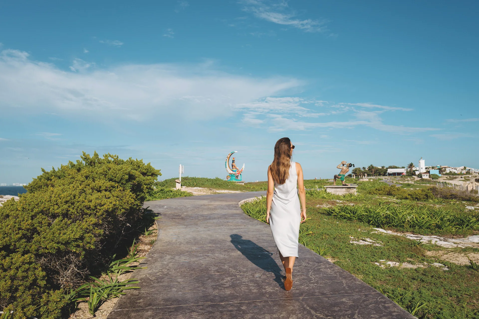 A woman walks a coastal path near Almare, a Luxury Collection Resort, Isla Mujeres, under a blue sky.