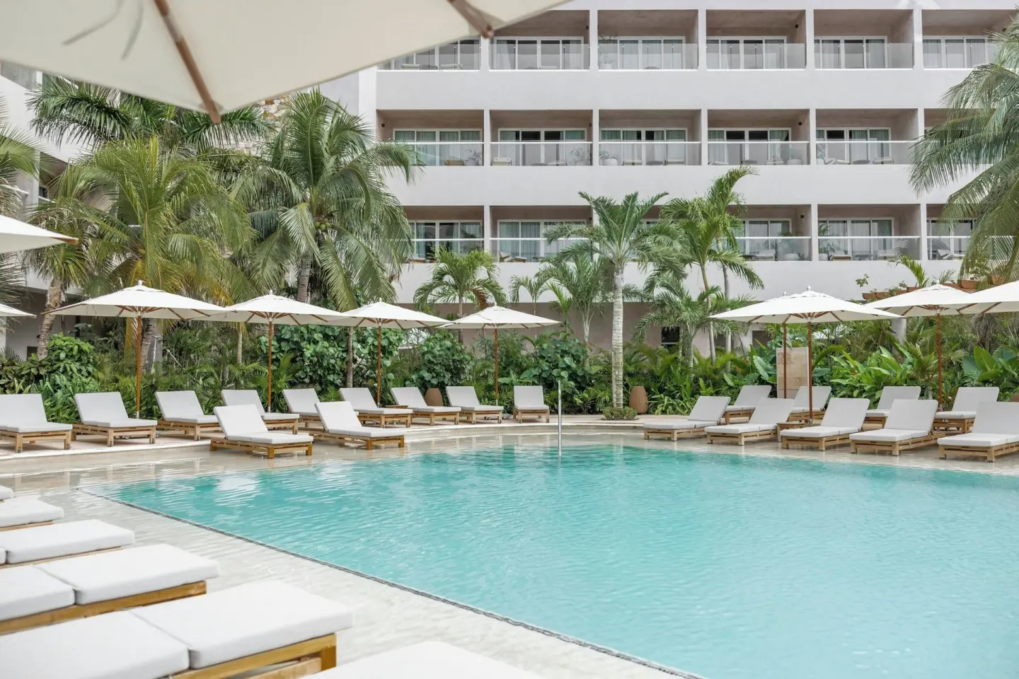 Resort pool with loungers, palms and guest room balconies at Almare, a Luxury Collection Resort, Isla Mujeres.