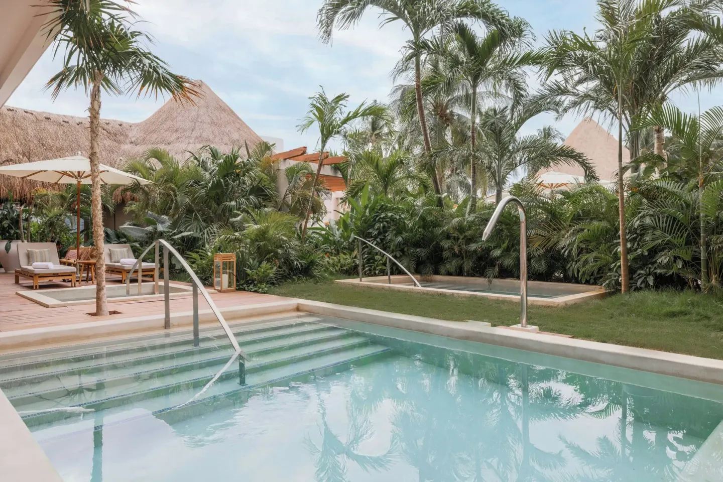 A garden pool with steps, palms, and thatched roofs is shown at Almare, a Luxury Collection Resort, Isla Mujeres.
