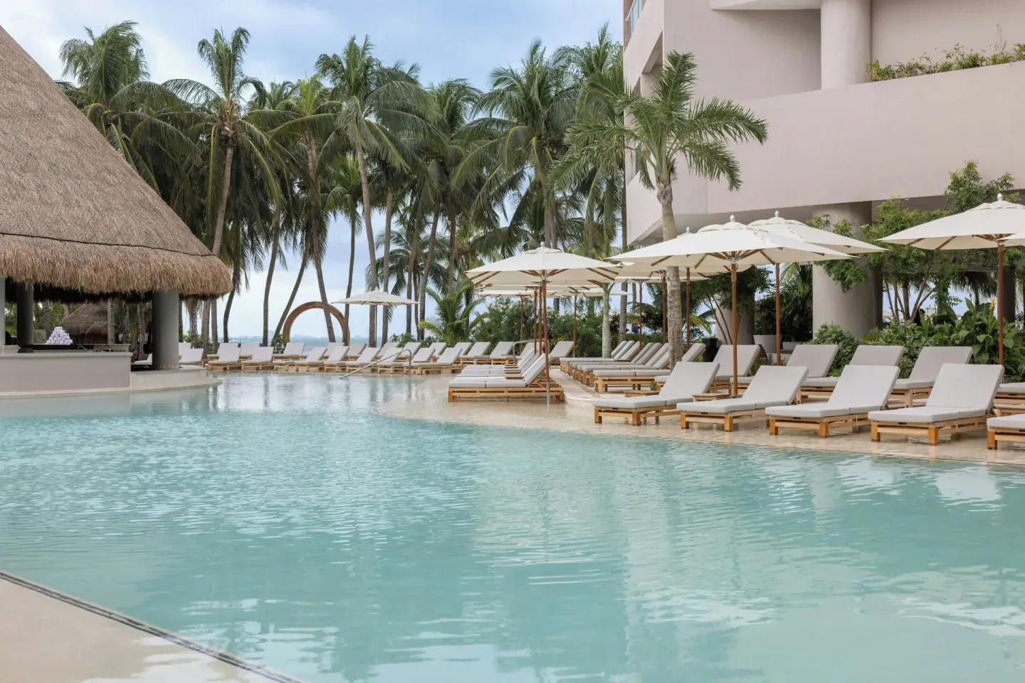 Pool deck with palapa-roof bar, loungers, and palm trees at Almare, a Luxury Collection Resort, Isla Mujeres.