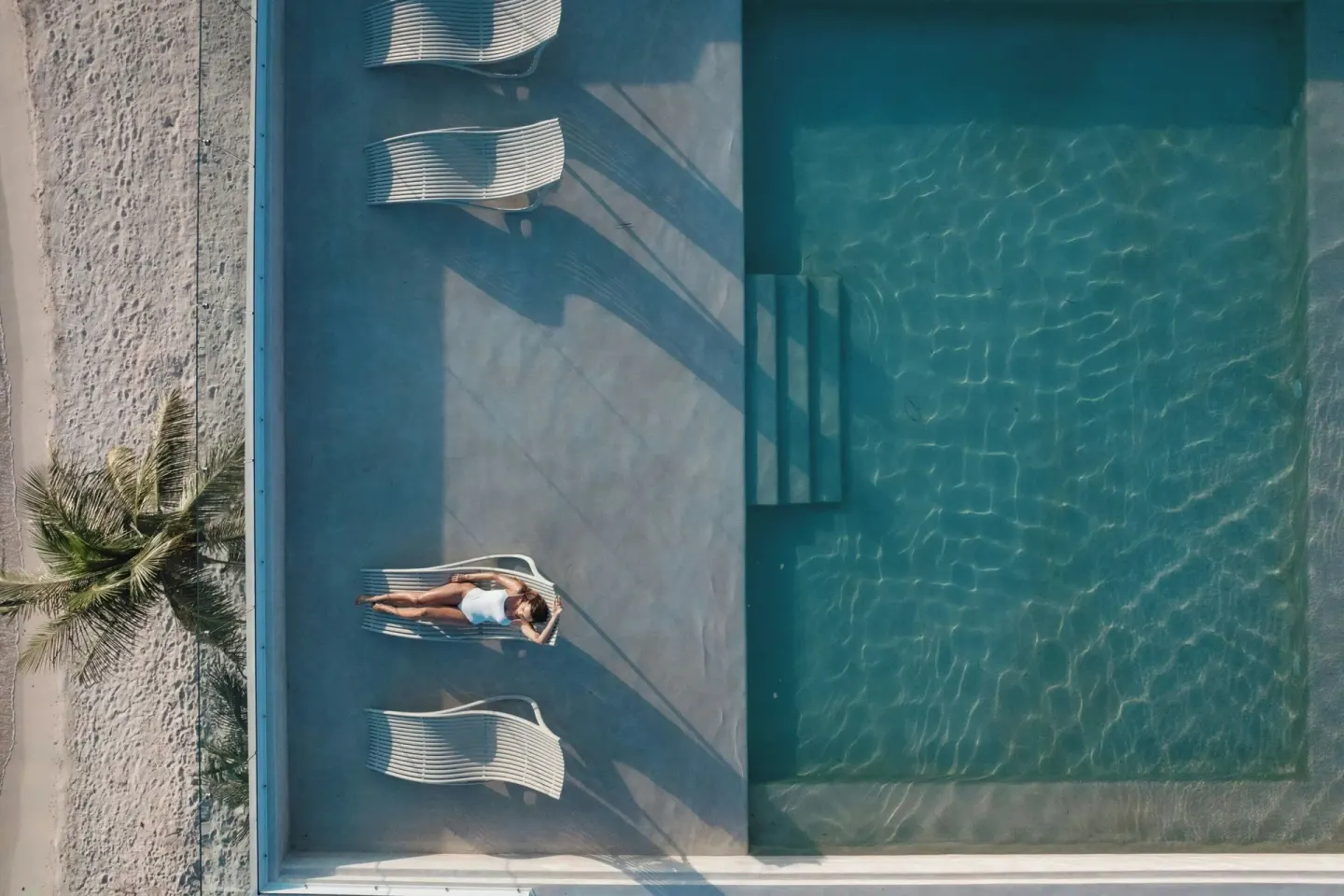 Overhead view of a guest sunbathing by a rectangular pool at Almare, a Luxury Collection Resort, Isla Mujeres.