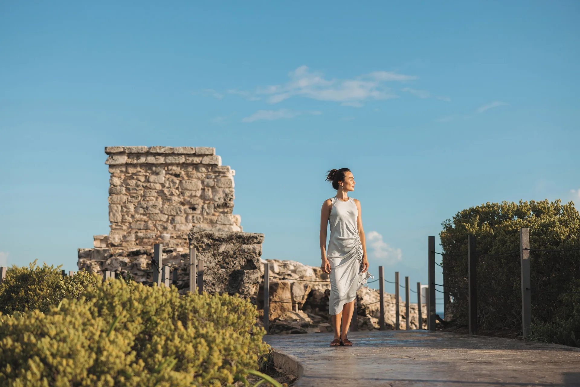 A woman walks past stone ruins near Almare, a Luxury Collection Resort, Isla Mujeres, on a sunny path.