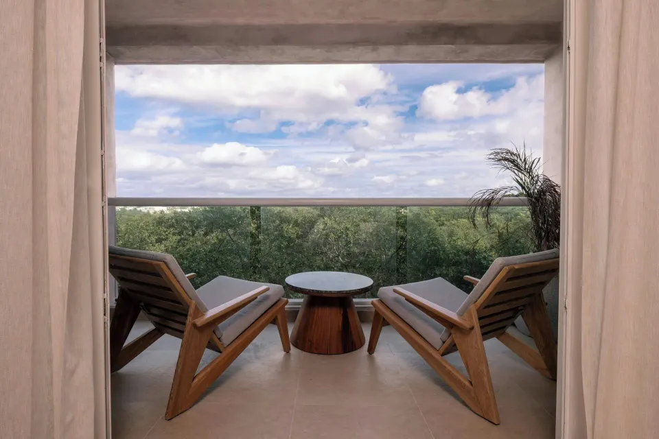 Standard Room Balcony seating with glass railing and treetop view at Almare, Isla Mujeres.