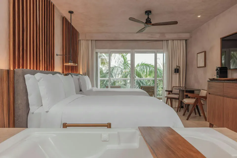 Standard Room Balcony with two beds, tub edge, and palm-facing windows at Almare, Isla Mujeres.