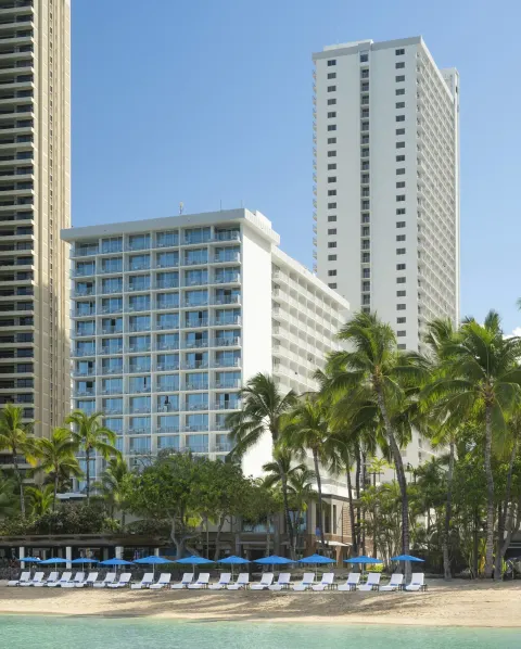 Beachfront hotel towers and lounge chairs at 'Alohilani Resort Waikiki Beach.