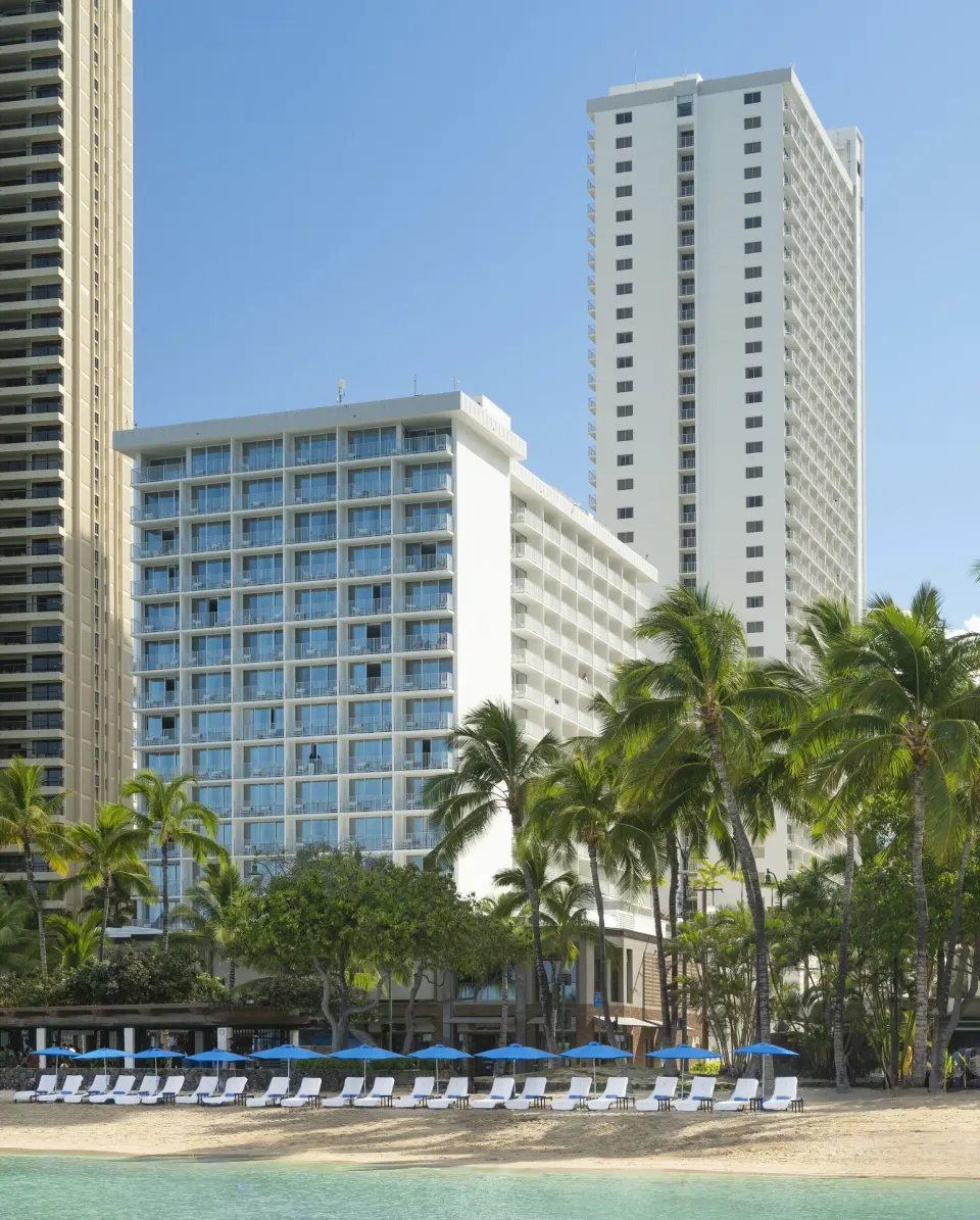 Beachfront hotel towers and lounge chairs at 'Alohilani Resort Waikiki Beach.
