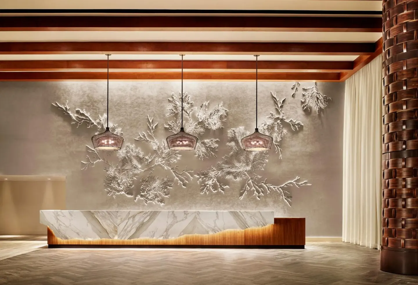 Reception desk with coral wall art and pendant lights at 'Alohilani Resort Waikiki Beach.