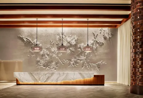 Reception desk with coral wall art and pendant lights at 'Alohilani Resort Waikiki Beach.