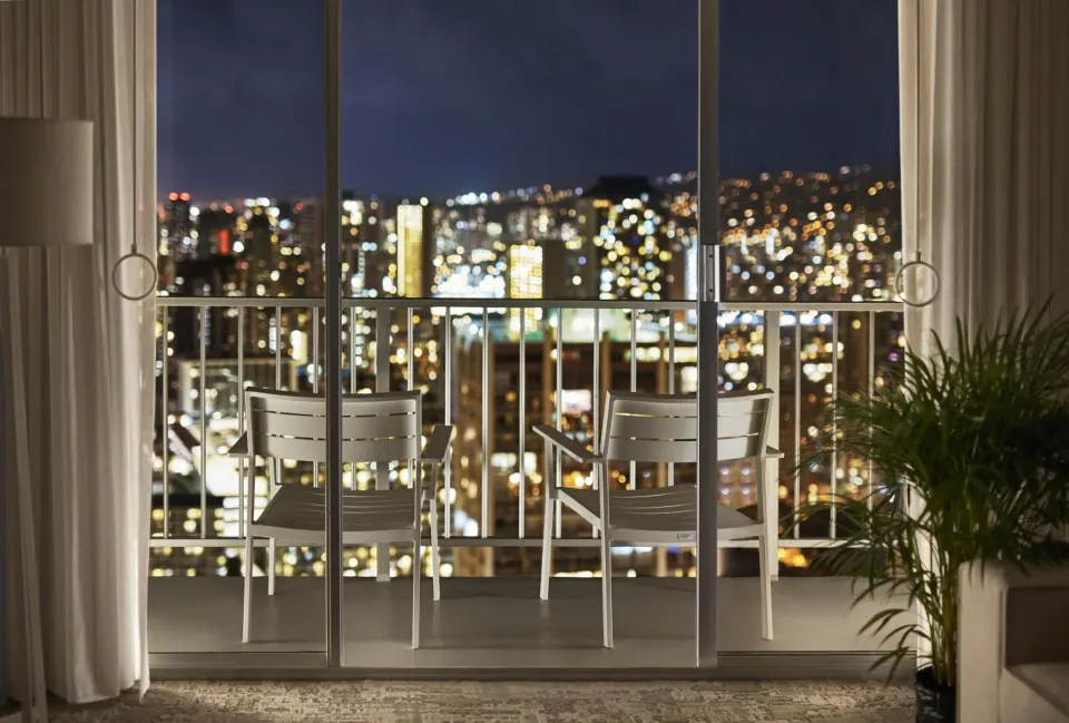 Balcony chairs and nighttime city view from a room at 'Alohilani Resort Waikiki Beach.